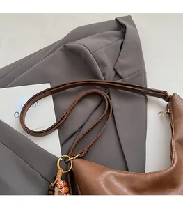 Detail of a brown leather crescent shoulder bag with a colorful beaded charm and metal buckle