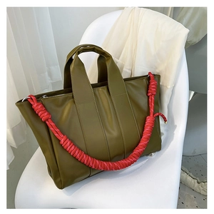 Dettaglio della borsa tote verde oliva con corda decorativa rossa e bianca su sedia