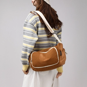 Rear view of model wearing a large brown crossbody travel bag with white zipper trim