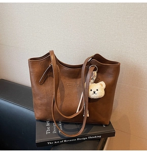 Detailed view of brown leather tote bag with lychee texture and plush bear accessory