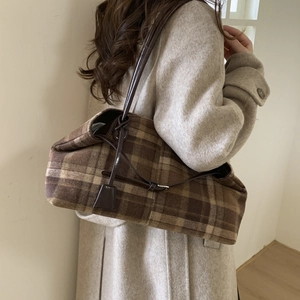 Close-up of vintage brown plaid tote bag with slim leather straps on beige coat