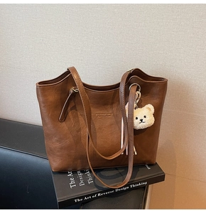 Detail of a dark brown matte tote bag featuring printed text and a cute bear charm