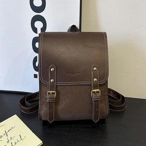 Detail of vintage brown leather backpack featuring golden buckles and embossed brand logo