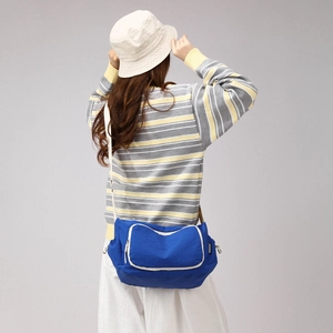 Detail view of large blue nylon crossbody bag with white trim worn by a model