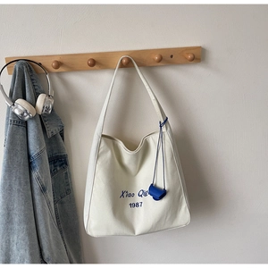 Dettaglio della borsa tote in tela bianco sporco con stampa Xiao Qi 1987 e mini ciondolo