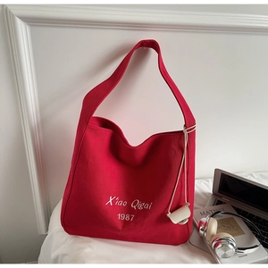 Dettaglio della borsa tote in tela rossa con ricamo bianco e piccolo ciondolo bianco