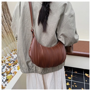 Detail of a pleated dark brown crescent bag worn by a model in an autumn setting