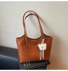 Detail of a brown leather tote bag with brand logo and a cute white plush bear charm