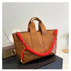 Dettaglio della borsa tote in pelle caramello con tracolla in spessa corda intrecciata rossa
