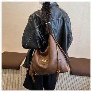 Close-up of a vintage dark brown leather tote bag featuring a gold metal M logo detail