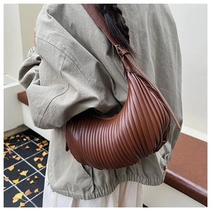 Brown pleated hobo bag worn as a shoulder bag against a minimalist studio background
