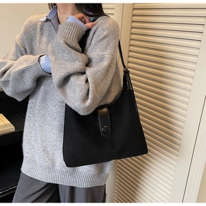 Model wearing a black matte and glossy leather shoulder bag with buckle detail