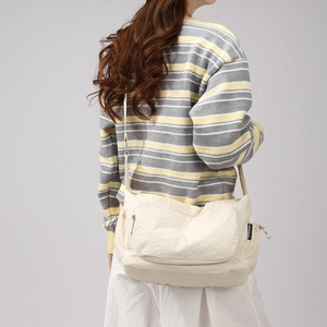 Detailed side view of cream-colored nylon crossbody bag with spacious zipper pocket