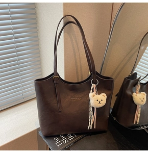 Detail of dark brown faux leather tote bag with brand logo and cute plush bear charm