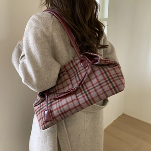 Plaid wool tote bag with dark red straps shown on shoulder with a beige coat