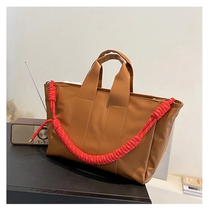 Dettaglio borsa shopper marrone con tracolla intrecciata rossa e trama in pelle