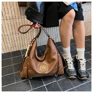 Détail d'un sac Hobo en cuir marron avec un grand logo M doré et un pendentif en perles