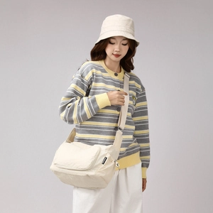 Detail of a beige canvas crossbody bag with adjustable wide strap and side brand tag