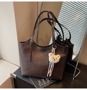 Detail of dark brown leather tote with golden buckle and cute plush bear accessory