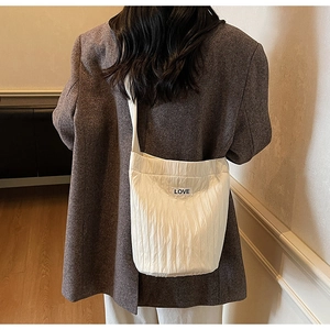 Model wearing a cream white pleated bucket bag with LOVE patch on dark grey blazer