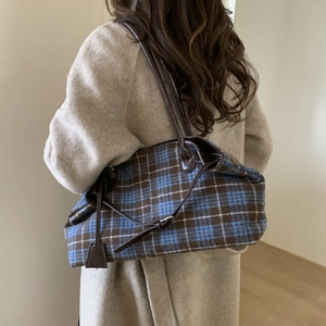 Detail of blue and brown plaid tote bag in wool fabric worn on shoulder by model