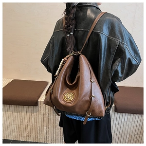 Détail d'un sac à dos marron en similicuir avec logo M métallique et pendentif en perles