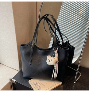 Detail of black tote bag with gold logo, teddy bear charm and striped ribbon accent