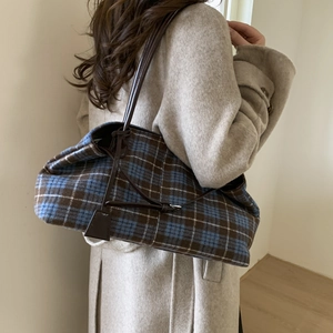 Close-up of a large blue plaid tote bag with brown leather straps on a wool coat
