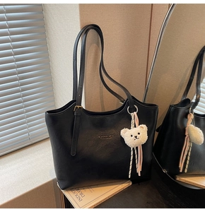 Detail shot of black leather tote bag with adjustable straps and white teddy bear charm