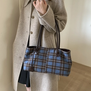 Detail of plaid tote bag with brown leather handles worn by a model in an autumn coat