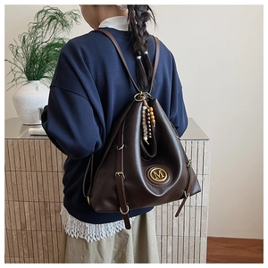 Détail d'un grand sac à dos en similicuir marron foncé avec logo M doré et perles décoratives