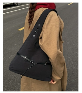 Outdoor street style view of large black shoulder bag with silver eyelets and wide strap