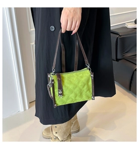 Detail of green quilted handbag featuring a dark brown leather handle and silver metal lock