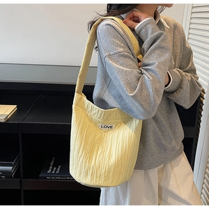 Close-up of quilted pale yellow bucket bag with vertical pleats and LOVE patch