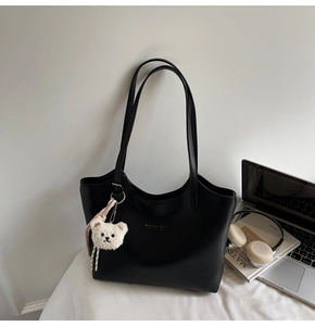 Close-up of black leather tote bag with gold logo and white teddy bear charm on white desk
