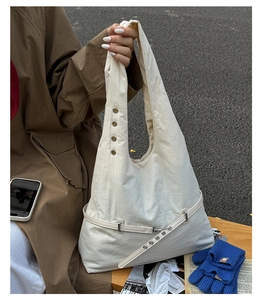 Detail of off-white canvas tote bag with metal eyelets and decorative leather strap
