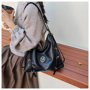 Détail du sac cabas en cuir noir avec logo M doré et boucle décorative sur le côté