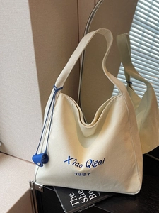 Borsa tote in tela crema con ricamo blu e ciondolo laterale in un set alla moda