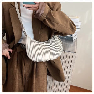 Close-up of cream pleated crescent bag worn with brown corduroy blazer for autumn