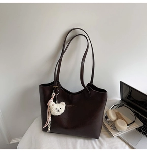 Detail of dark brown leather tote bag with gold logo and cute white plush bear pendant