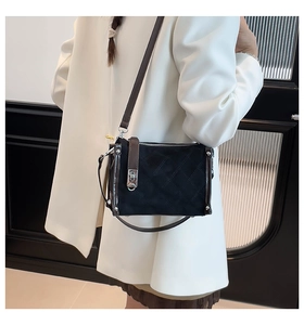 Detail of black quilted shoulder bag with brown strap and silver twist lock on a white suit