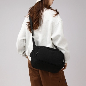 Side view of large black nylon crossbody bag worn by a model in a minimalist setting