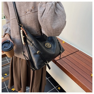 Détail du sac cabas en cuir noir avec logo M doré et accessoire de charme en perles de bois