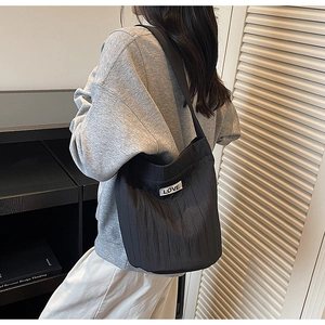Detailed back view of a black pleated tote bag with LOVE patch worn on the shoulder