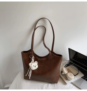Detailed view of brown leather tote bag with plush bear charm and sleek golden logo