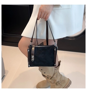 Detail of black quilted square handbag with silver buckle and brown trim on a white dress