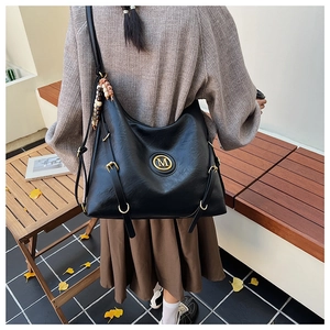 Détail du sac hobo en similicuir noir avec logo M doré et pompon perlé sur une chaise extérieure