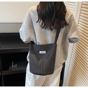 Detail of black pleated shoulder bag with white LOVE patch in a minimalist home setting