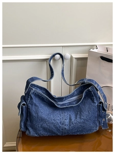 Detail of dark blue denim hobo bag featuring side flap pockets and metal eyelet strap