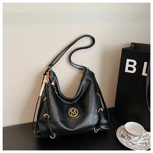 Détail du sac Hobo noir avec logo M doré, breloque perlée et texture cuir lisse